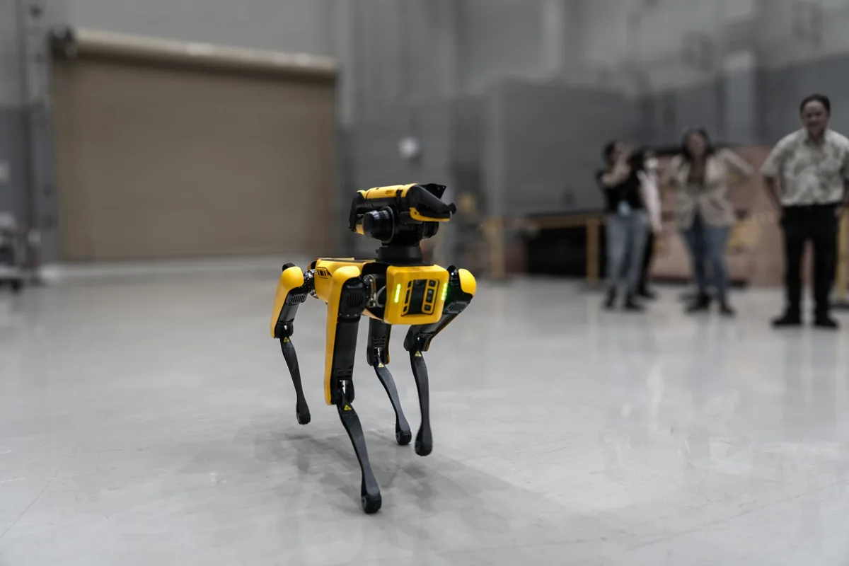 Yellow Spot quadruped robot carrying a sensor head during a demonstration inside a Pearl Harbor shipyard building
