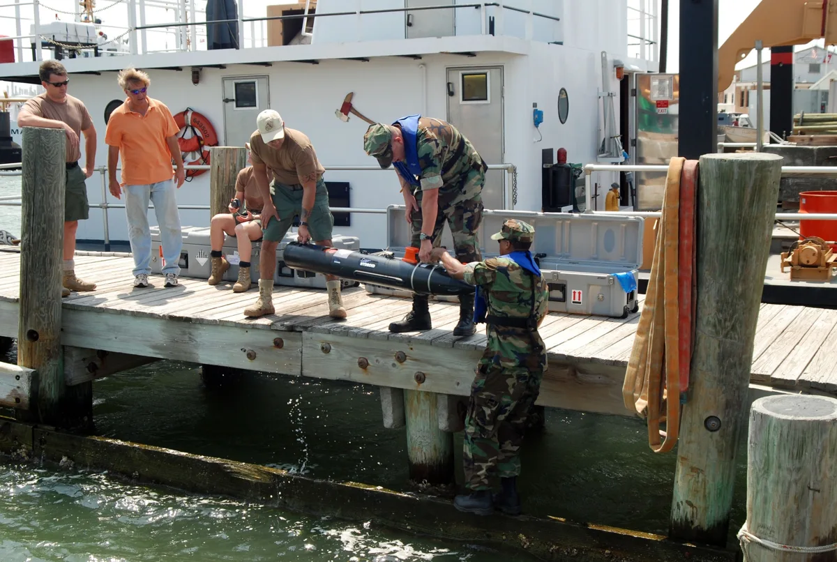 U.S. Navy personnel preparing a cylindrical underwater vehicle for launch from a dock in Corpus Christi